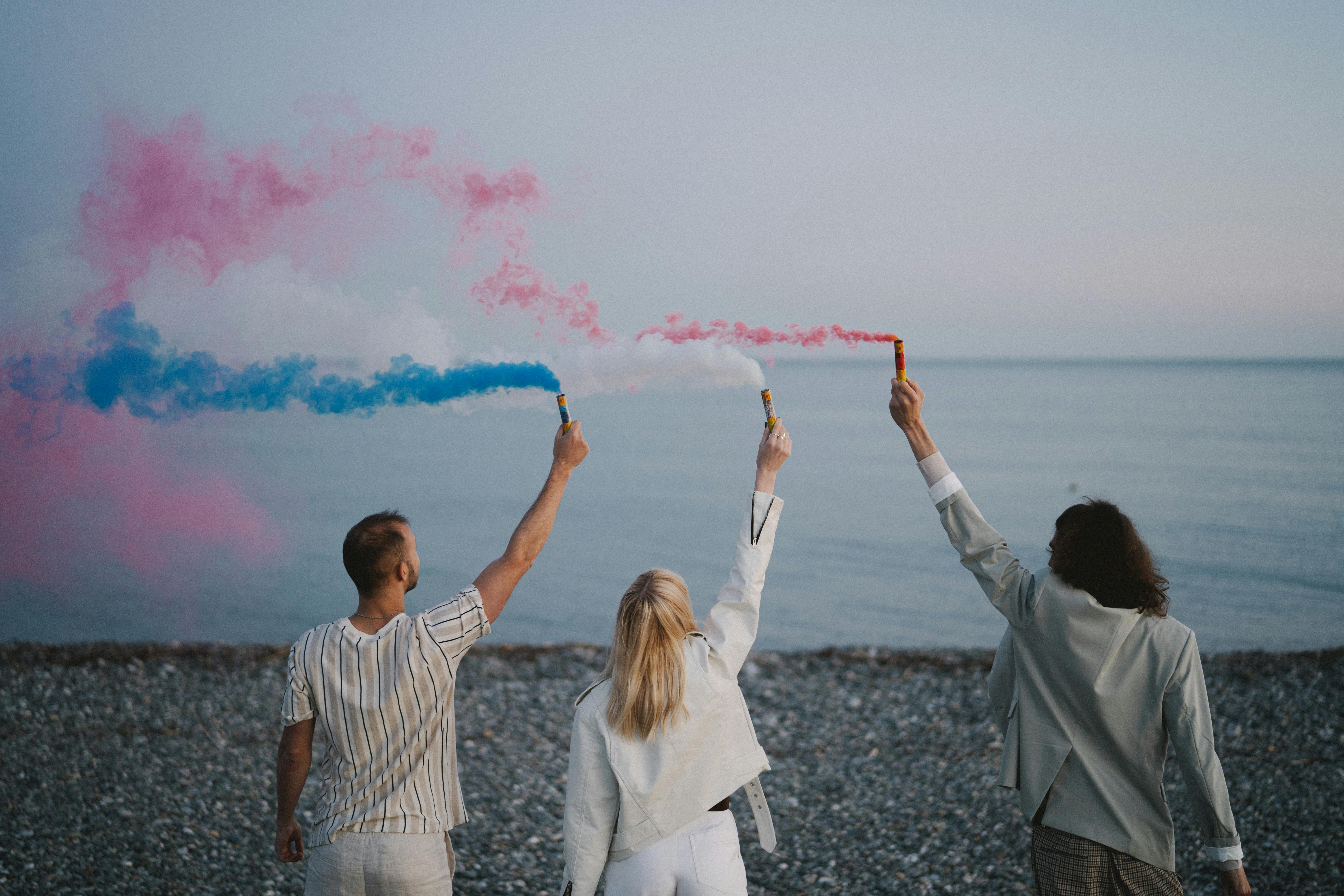 People Holding Colored Smoke Bombs on a Shore · Free Stock Photo