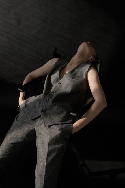 Stylish woman posing elegantly in grey suit, leaning back in a studio setting.