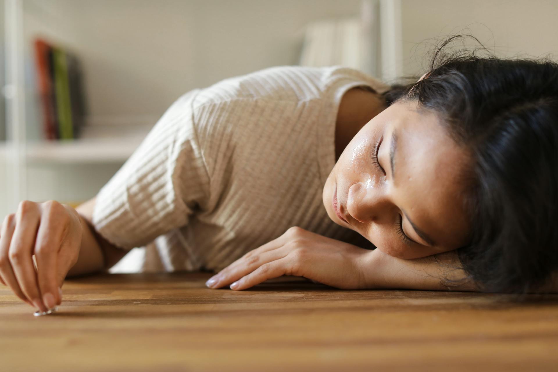 A Sad Woman Looking at the Ring she is Holding while Lying Her Face on a Wooden Surface