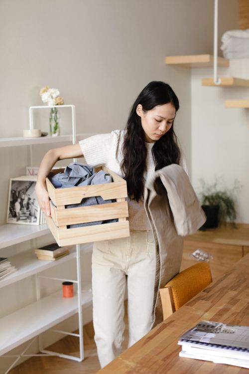 Free Asian woman arranging clothes in a wooden crate in a well-lit modern interior. Stock Photo