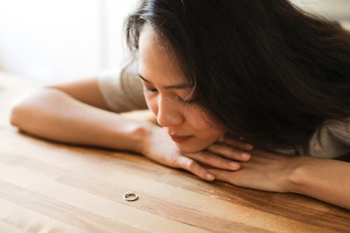 Free A Woman Crying Near the Wooden Table while Looking at the Ring Stock Photo