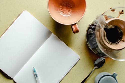 A Blank Notebook Beside Empty Cup and Coffee Maker