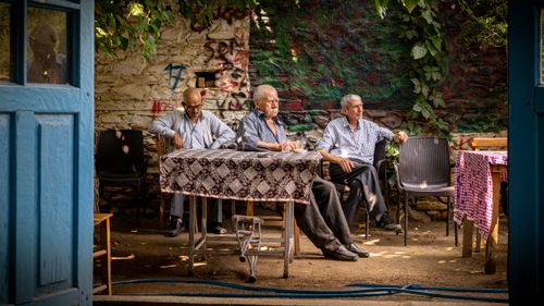 Free Three elderly men sitting at an outdoor cafe table, enjoying a sunny day. Stock Photo