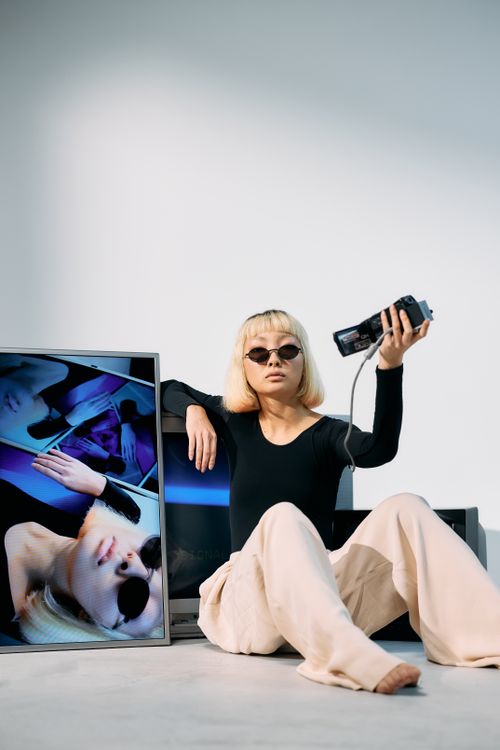 Free Trendy woman with blonde hair and sunglasses posing with a video camera, showcasing style and technology. Stock Photo