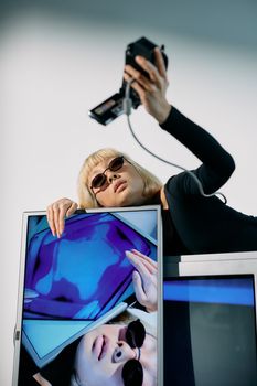 Fashion model takes edgy selfie with retro camera and screen, blending style and technology.