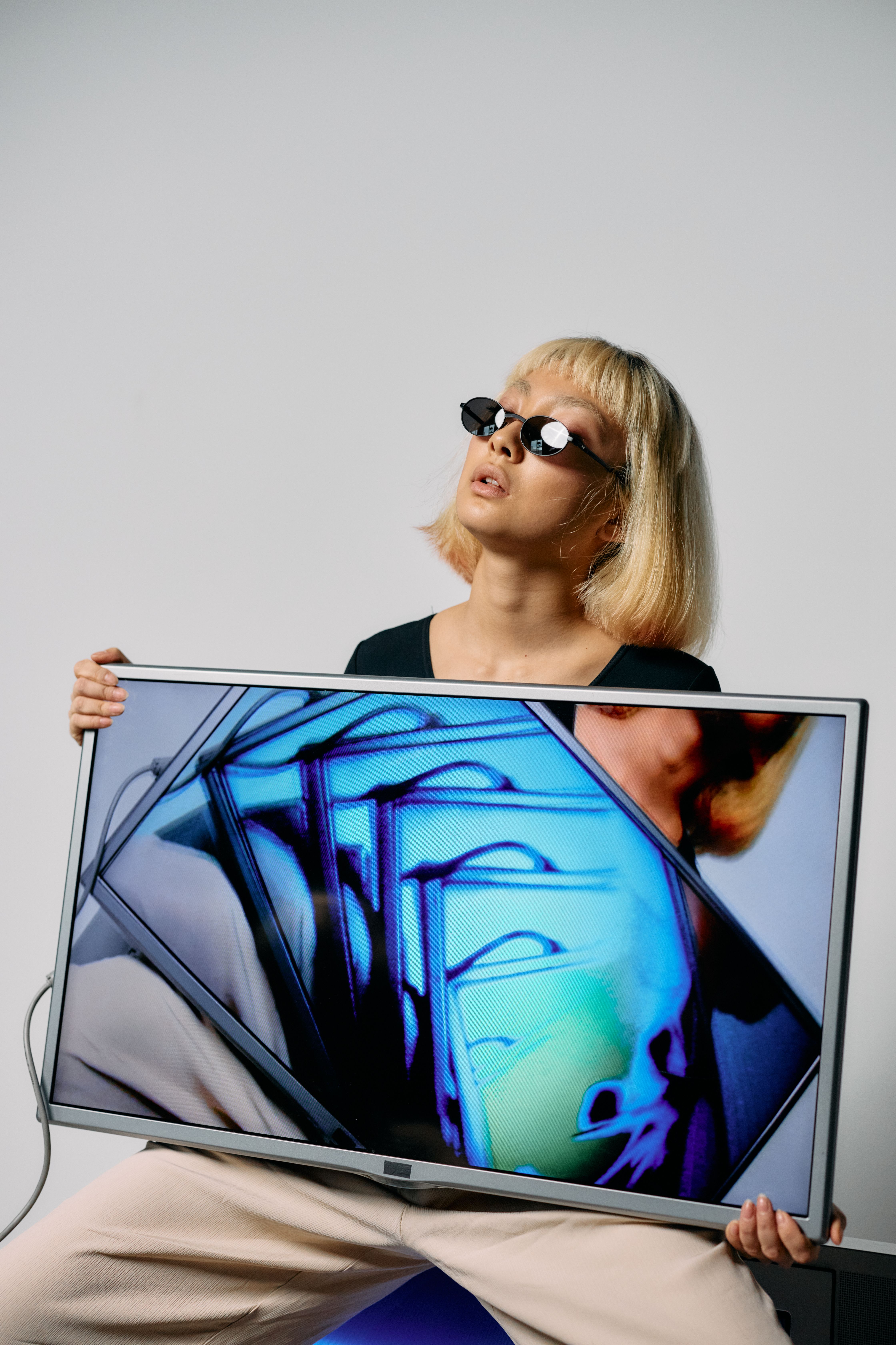 Fashionable woman wearing sunglasses holds TV with vibrant abstract art.