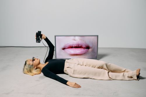 Free Fashionable model with eyewear posing alongside a video screen in a studio setting, blending style with technology. Stock Photo