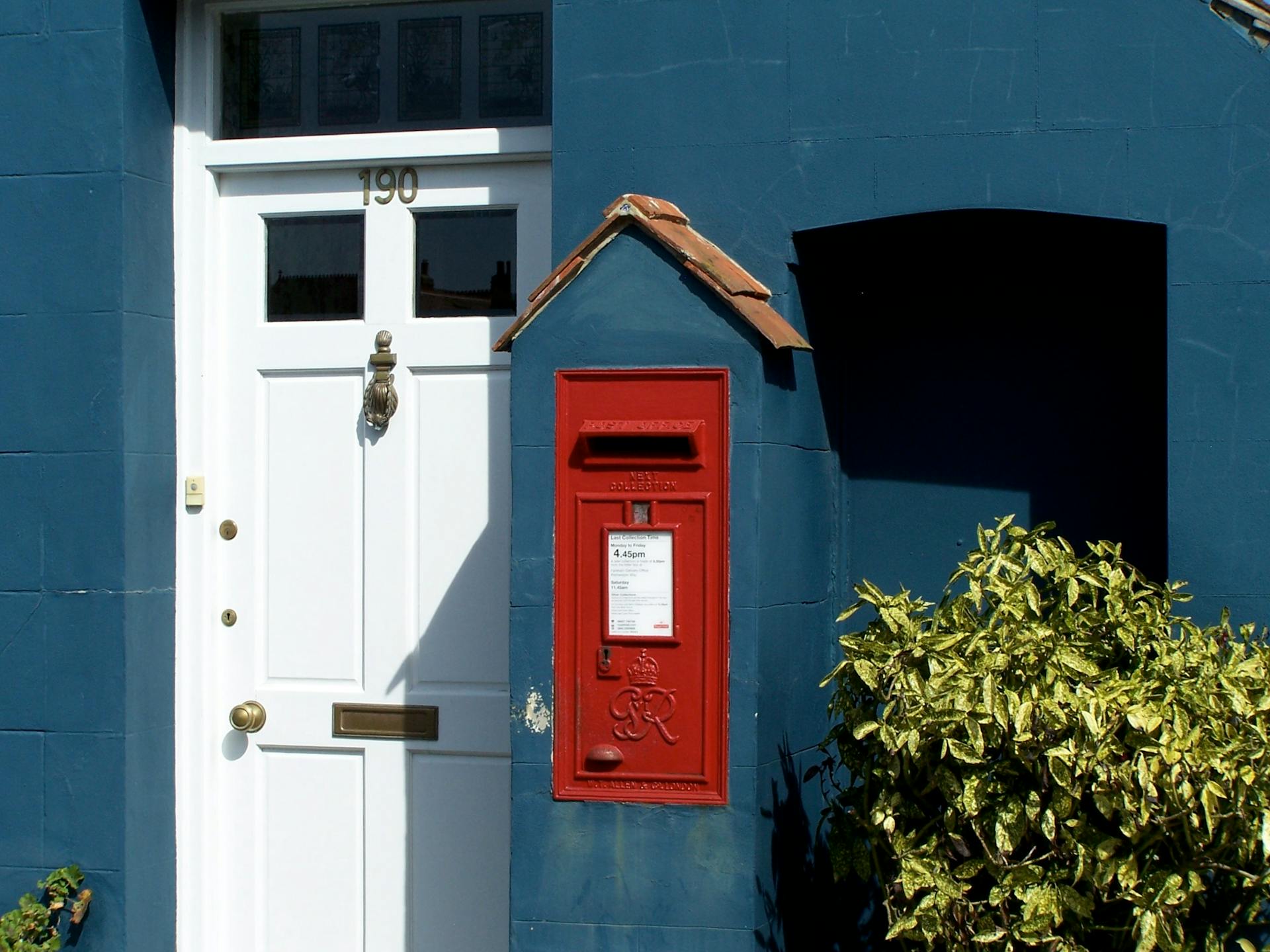 A striking red mailbox mounted on a blue wall beside a white door.