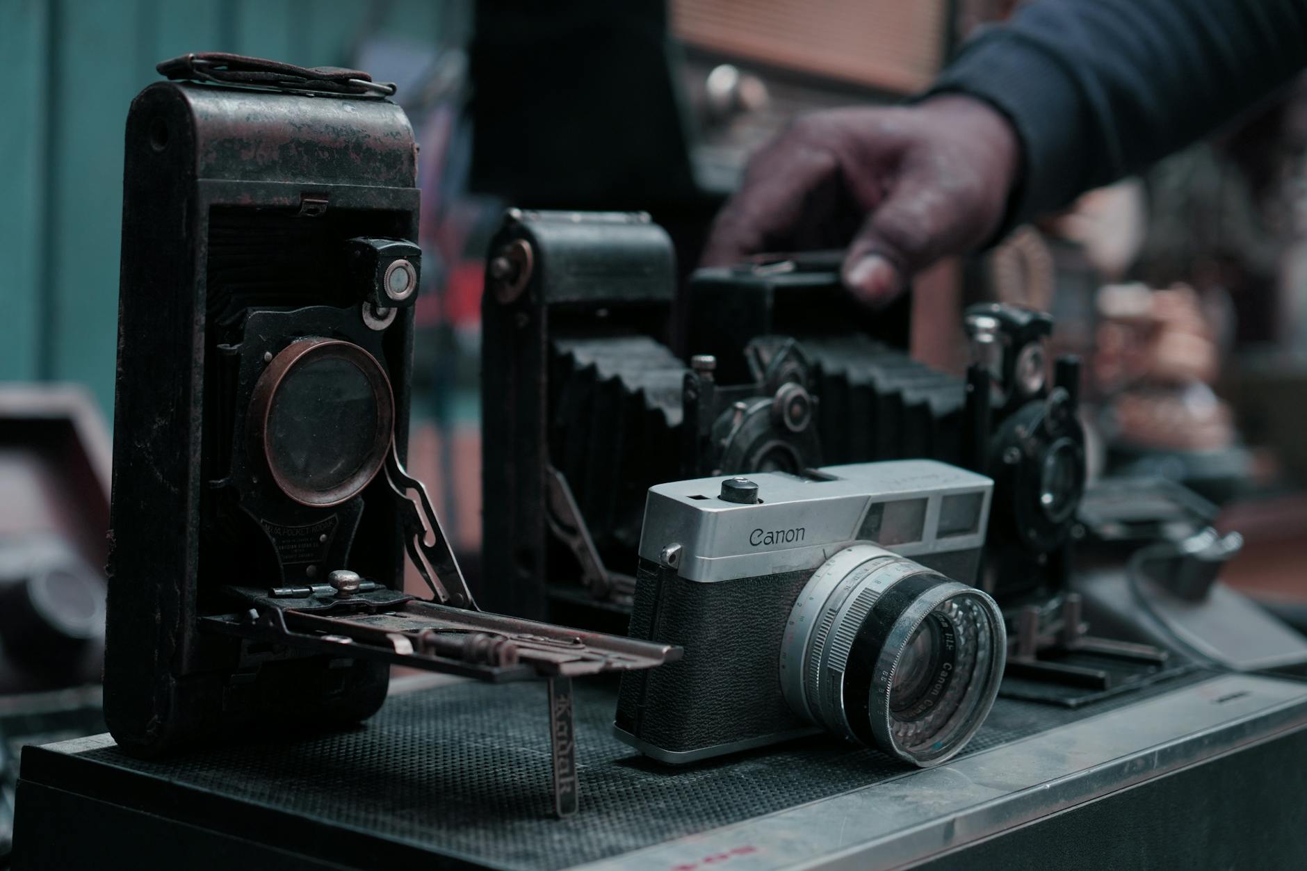 Close-up of various vintage cameras displayed with a hand gently touching them.