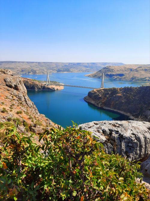 Free Scenic view of a bridge over a canyon with clear blue water and rocky cliffs under a bright sky. Stock Photo