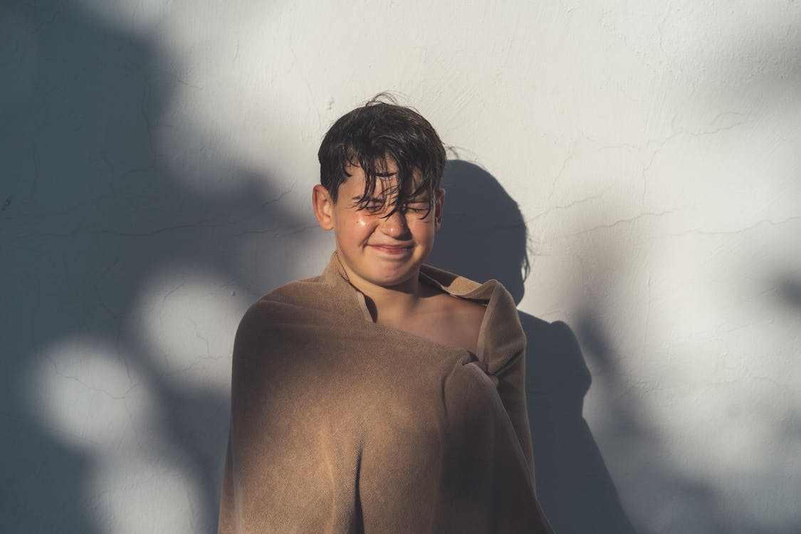 Boy with towel standing near white wall