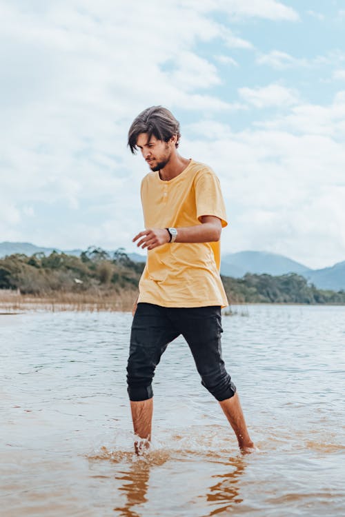 
A Man in a Yellow Shirt Walking on a Shore