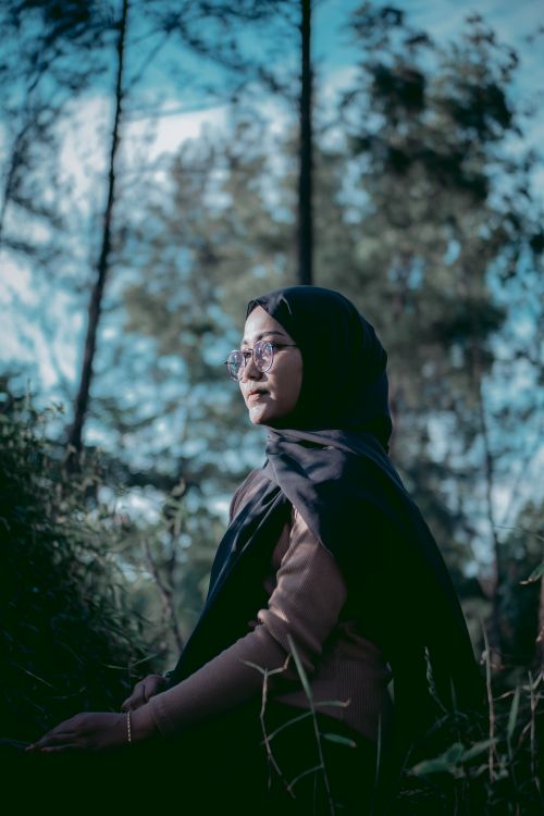 Free A serene portrait of a woman in a headscarf and eyeglasses in a lush outdoor setting. Stock Photo