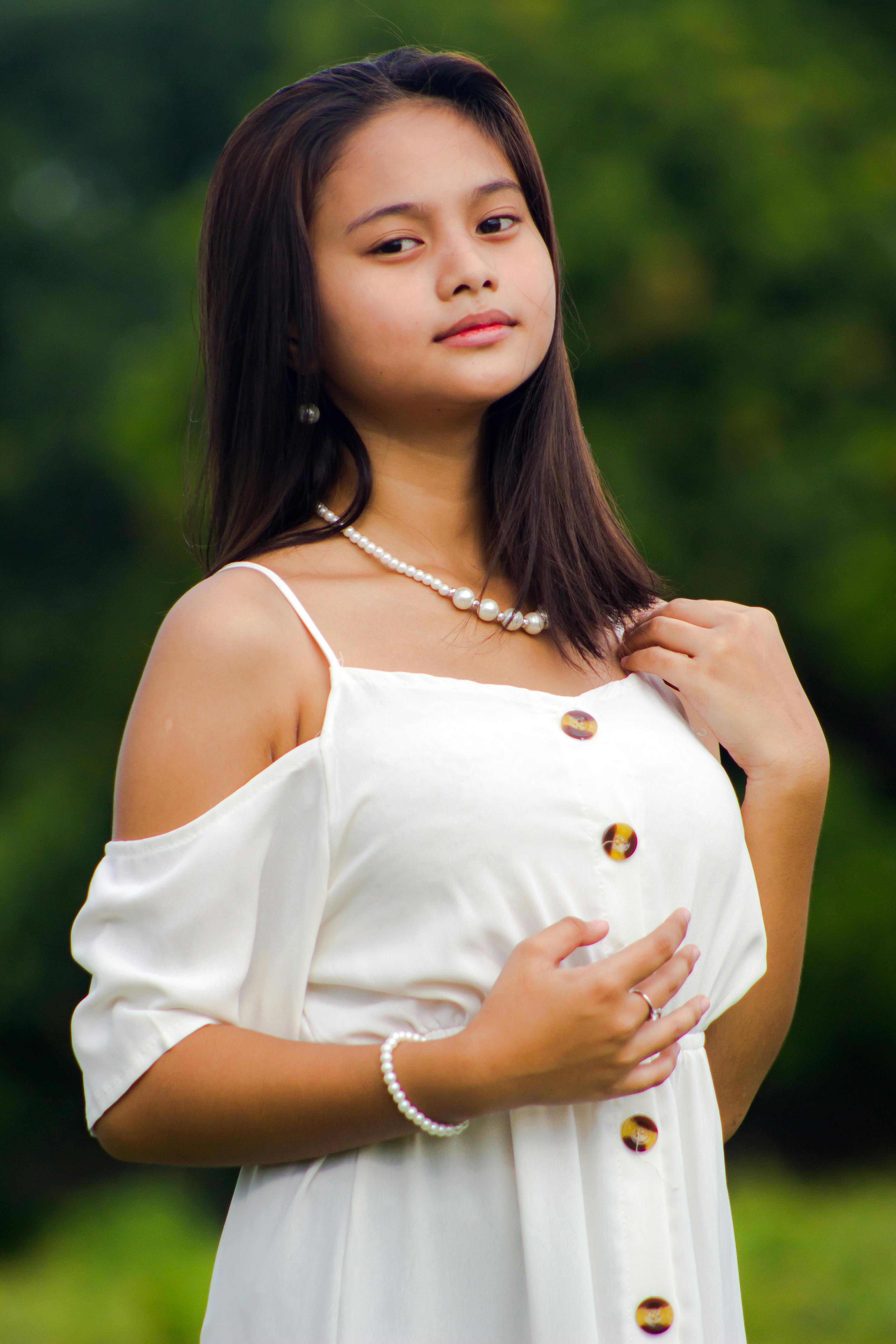 Portrait of a young woman in a white dress and pearl jewelry outdoors.