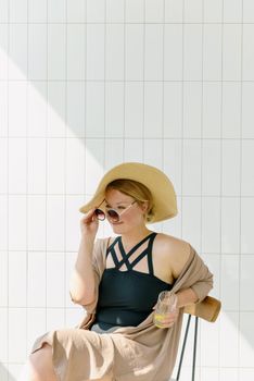 A woman wearing a sun hat and sunglasses enjoys a quiet moment indoors under natural daylight.