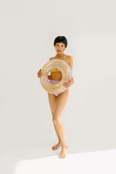 Asian woman in swimsuit holding a pink swim tube in a bright indoor setting.