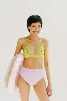 Cheerful woman in bikini holding an inflatable ring on a white background, exuding summer vibes.