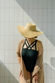 A woman posing in a stylish swimsuit and sun hat against a tiled wall, creating a chic summer look.