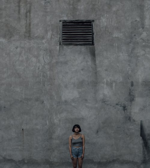 A Woman Wearing a Tank Top and Denim Shorts Standing in front of a Concrete Wall