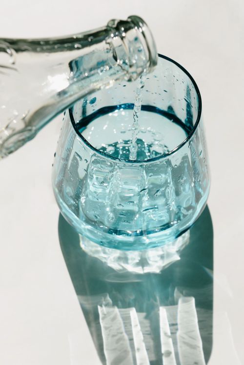 Free Close-up of water being poured into a textured glass with natural light casting shadows. Stock Photo