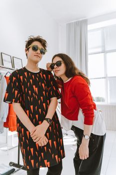 A fashionable duo, mom and teen, posing stylishly indoors, both wearing sunglasses.