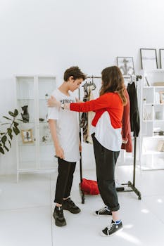 A mother helps her teenage son with his outfit in a stylish and modern fashion studio setting.