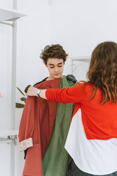 Woman in Red Long Sleeve Shirt Shopping For Clothes with a Young Man