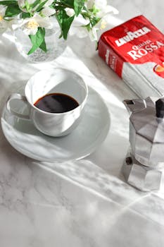 Elegant coffee scene with Lavazza packaging and floral decor on a marble tabletop.