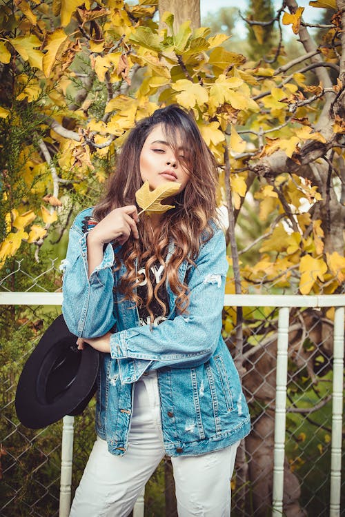A Woman in Denim Jacket Posing while Holding a Leaf