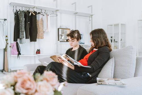 Free A mother and son reading magazines in a contemporary living room, surrounded by clothes and cozy decor. Stock Photo