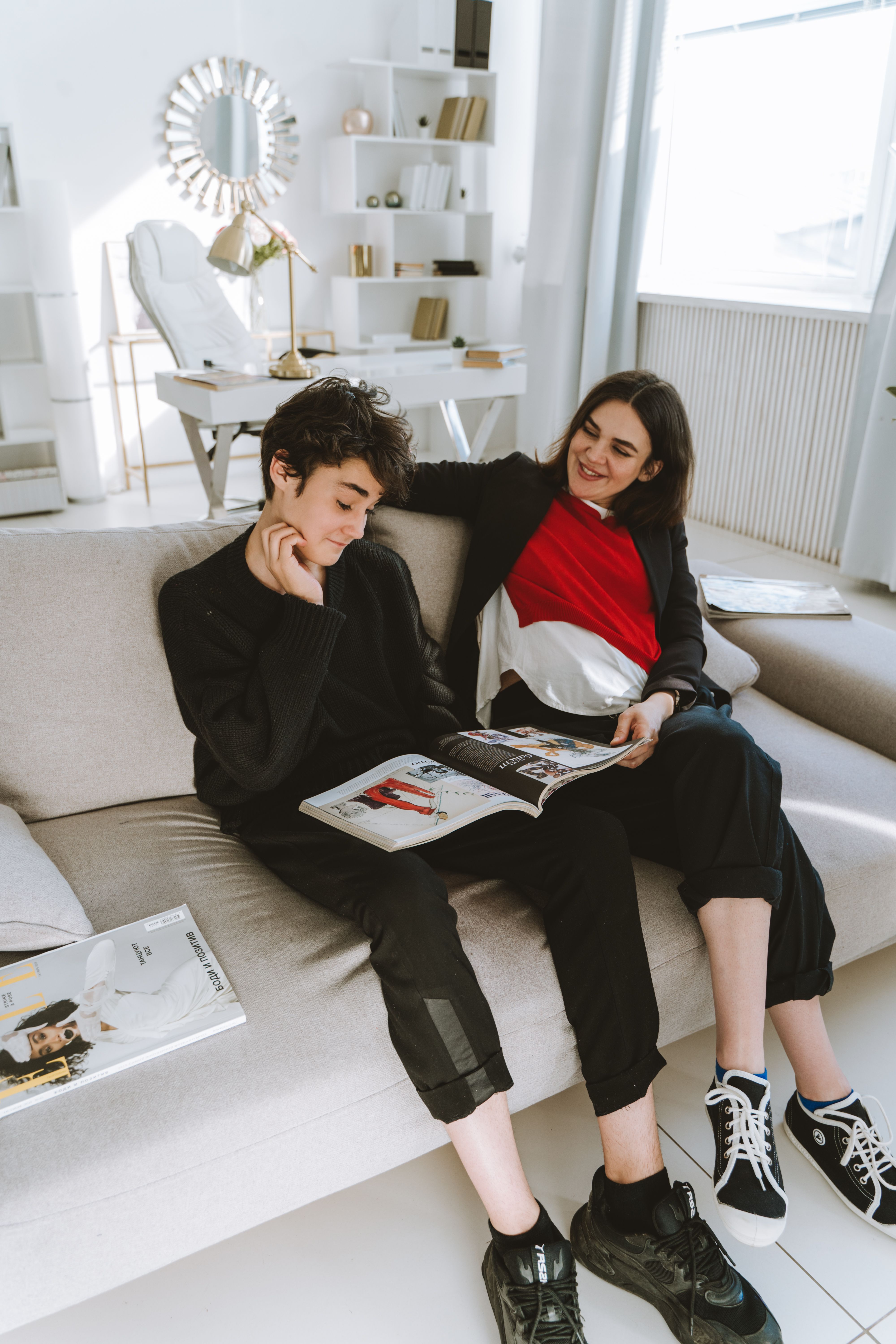 Mother and son enjoy casual reading time on a couch in a bright home office.