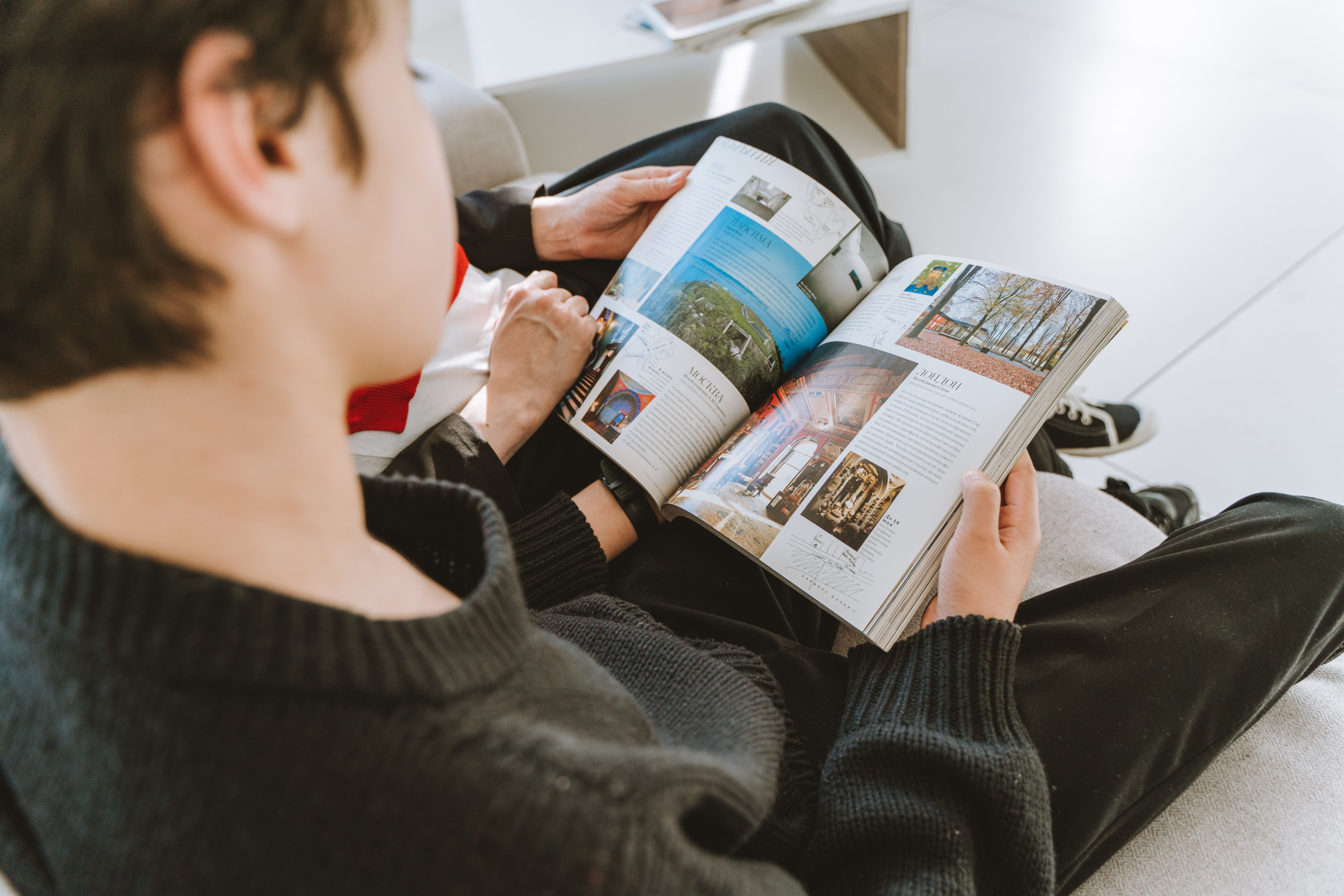 Young man in a cozy indoor setting reading a colorful magazine.