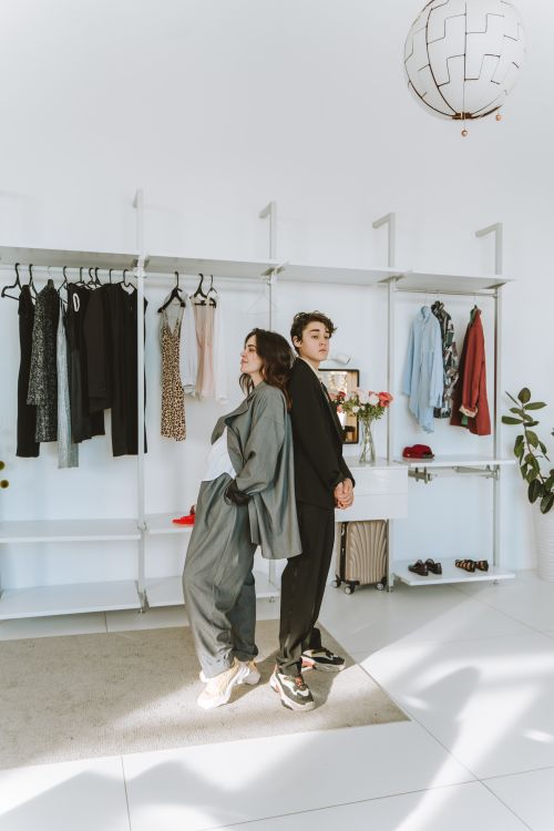 Free A mother and son stand back-to-back in a minimalist wardrobe, showcasing trendy urban fashion indoors. Stock Photo