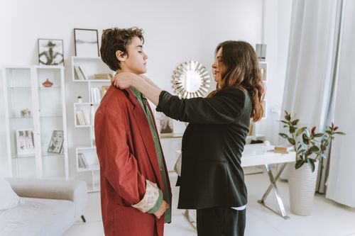 Free Woman adjusting her son's red coat inside a modern and elegantly decorated office space. Stock Photo