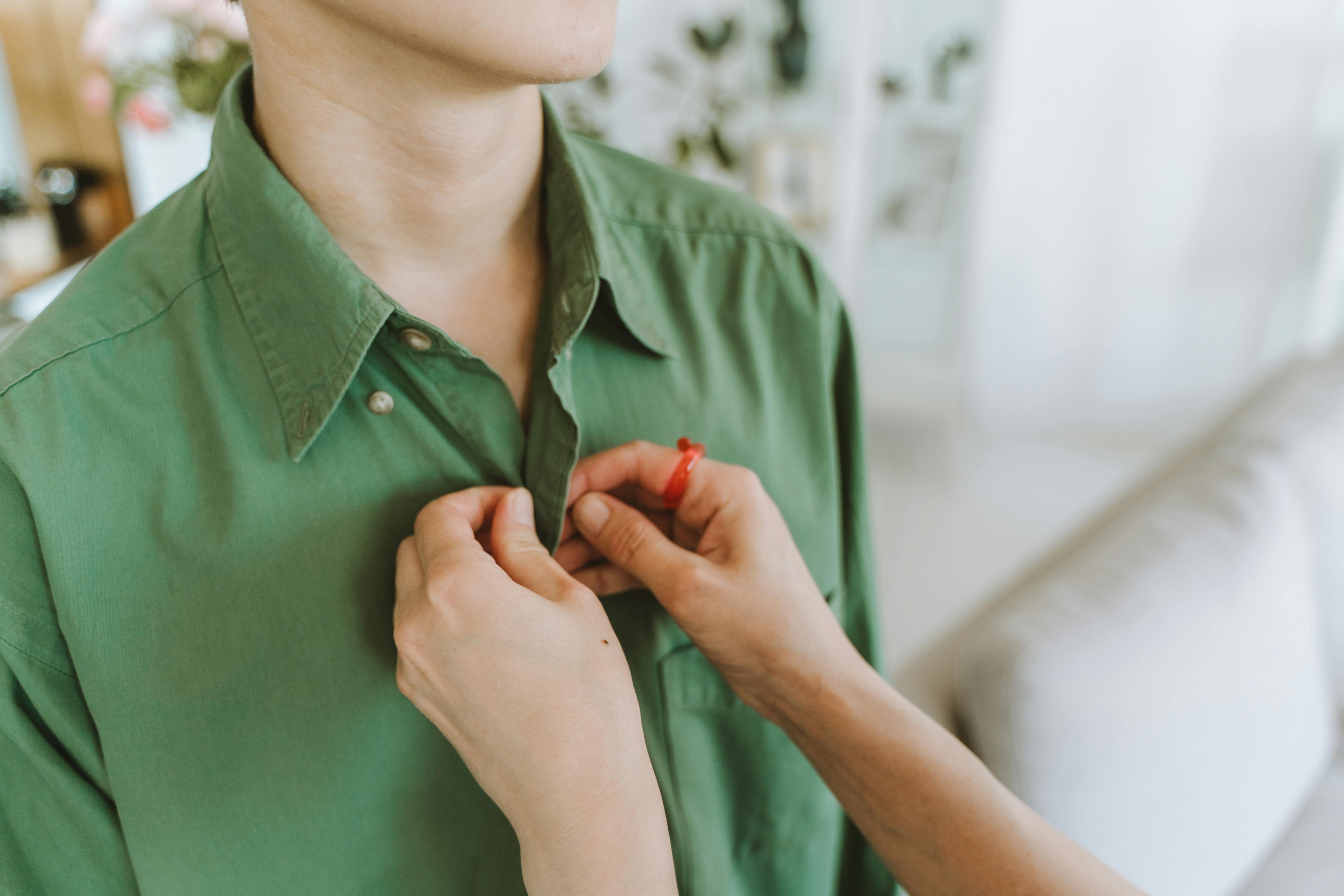 Detail shot of someone buttoning a green shirt, reflecting care and style.