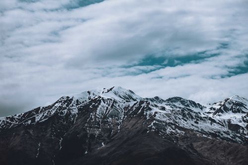 Free Majestic mountain range with snow peaks beneath a dynamic cloudy sky, perfect for nature lovers. Stock Photo
