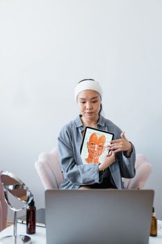 Woman presents skincare procedure technique using tablet in a home setting.