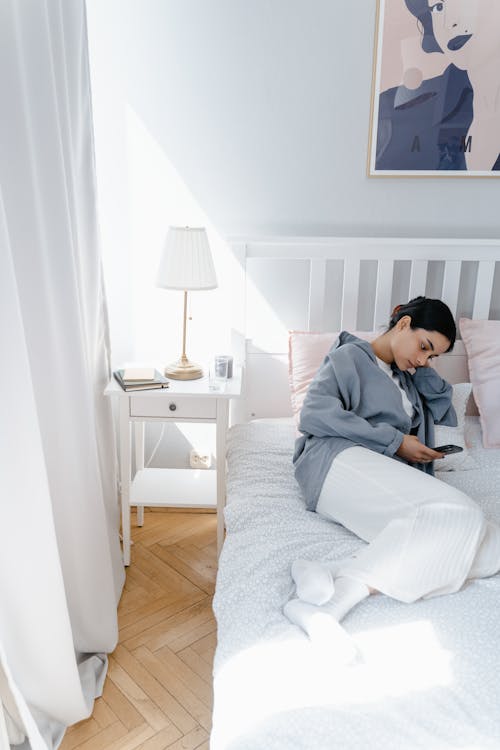 Free A Woman in Gray Long Sleeves Lying on the Bed while Using Her Mobile Phone Stock Photo