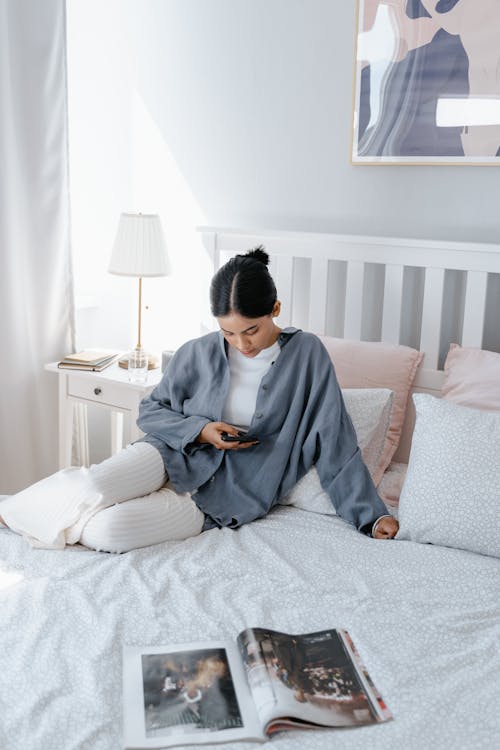 A Woman Sitting on Her Bed while Using Her Phone