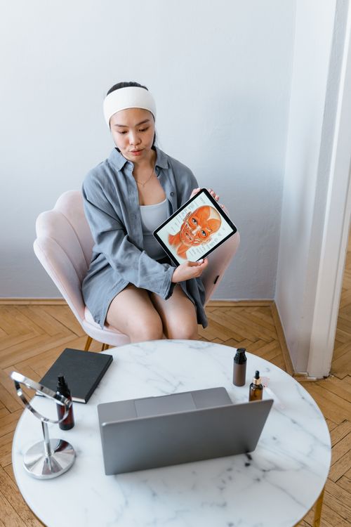 Free Woman demonstrating skincare procedure through a virtual consultation using a tablet. Stock Photo