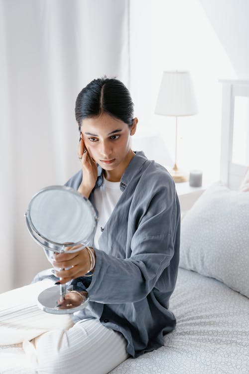 Free Woman Touching her Face while Looking at the Makeup Mirror Stock Photo