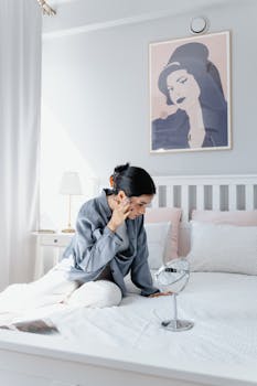 Adult woman sitting on bed engaged in relaxing skincare routine in a bright bedroom.