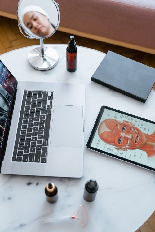 Free An overhead view of a tabletop with a laptop, tablet displaying human anatomy, and beauty products. Stock Photo