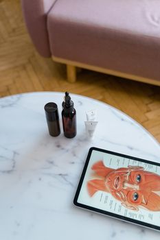 Cosmetic bottles and tubes on marble table beside anatomy diagram on tablet.