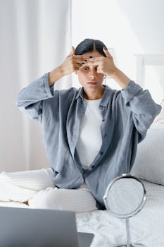 Adult woman focusing on facial skincare routine at home with mirror on bed.