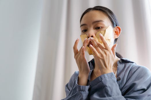 A woman applies a gold facial mask for skincare in an indoor setting.