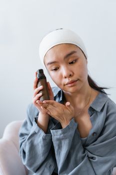 Young woman poses with skincare product indoors, focusing on beauty and wellness.