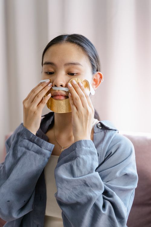 Free A young woman applies a gold facial sheet mask in a calming indoor setting. Stock Photo