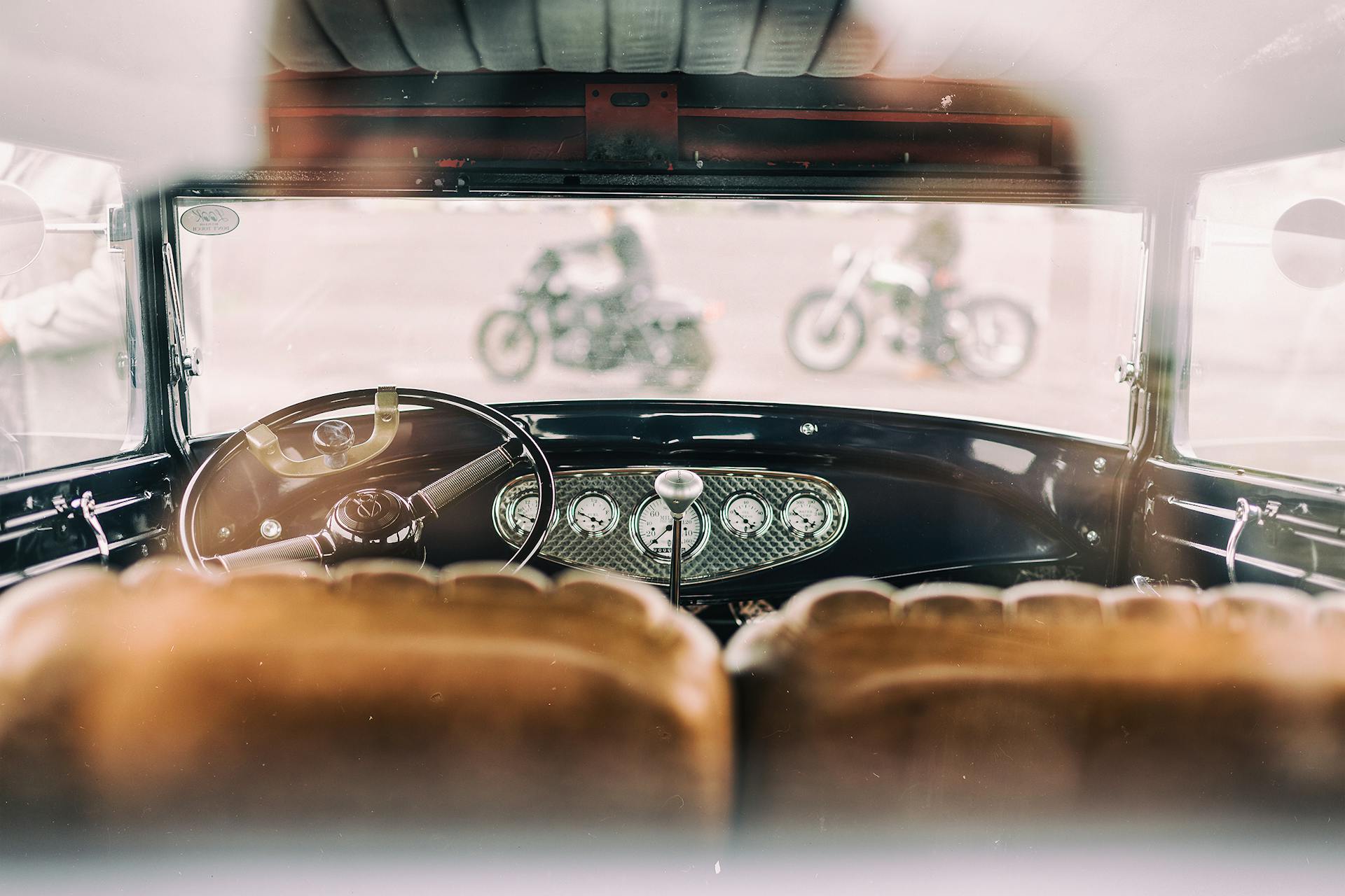 Classic vintage car interior with focus on dashboard and blurred motorcycles outside.