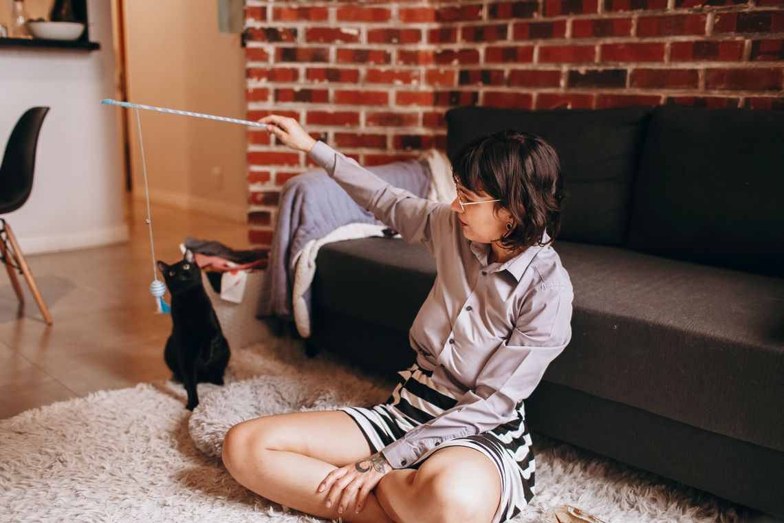 Woman playing gently with her black cat on a living-room floor